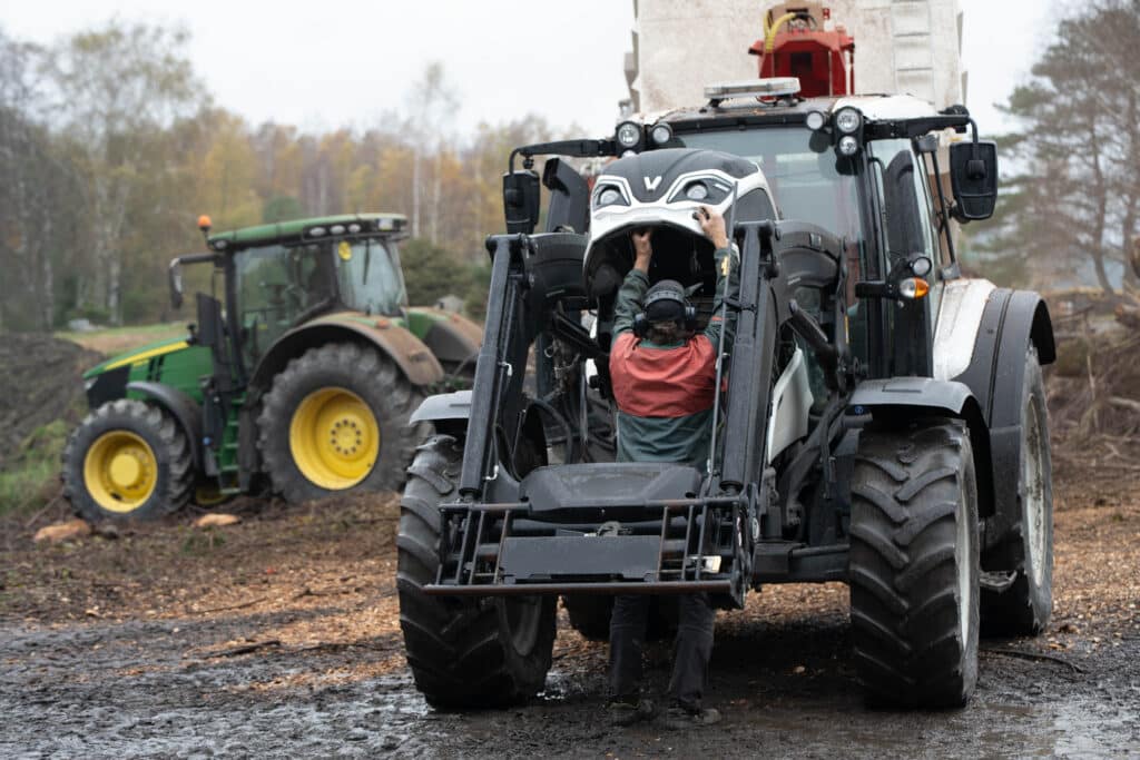 Förare kliver ur svart Valtra-traktor vid flisningsarbete i Hjälteby – John Deere i bakgrunden