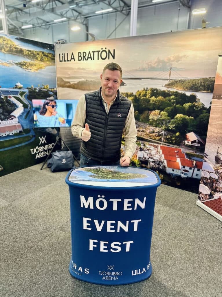 Magnus vid Tjörnbro Arenas mässmonter med drönarbild av Lilla Brattön i bakgrunden