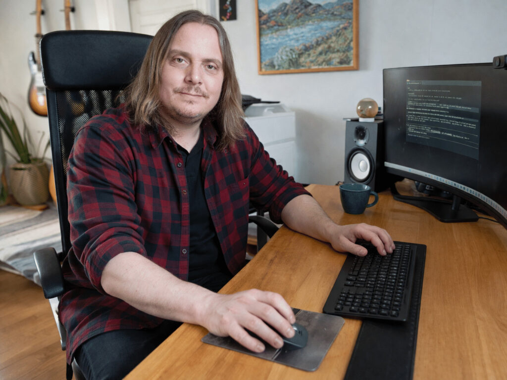 Patrik Jansson i flanellskjorta vid skrivbord, i rollen som grafisk designer på Grafikbyrån